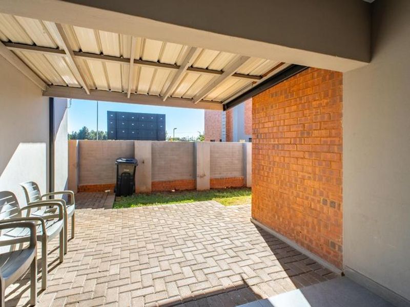 A covered patio area featuring paved flooring and a brick feature wall, providing a functional outdoor space for relaxation.