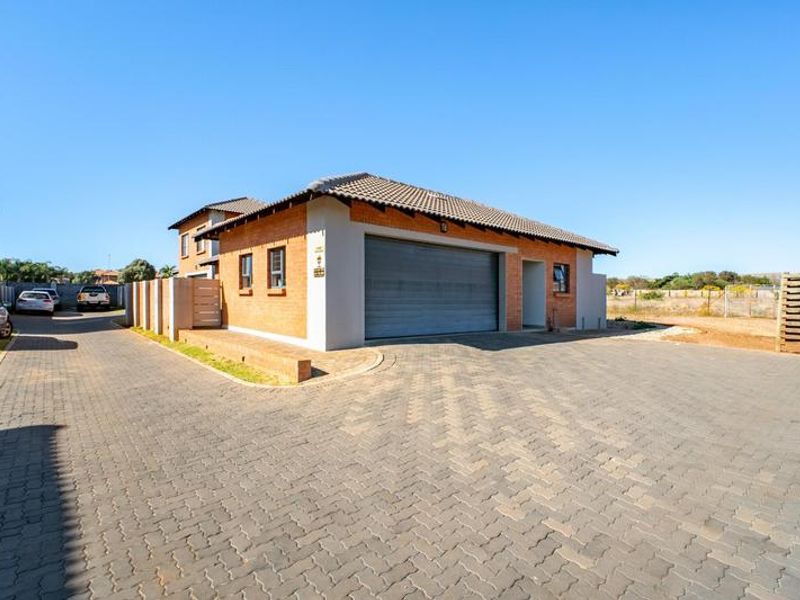Front exterior view of a townhouse featuring a brick facade, tiled roof, and a spacious paved driveway leading to an automated garage.