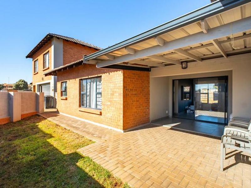 A covered brick-paved patio area adjacent to the townhouse, featuring a sliding glass door entrance and a small private garden space.
