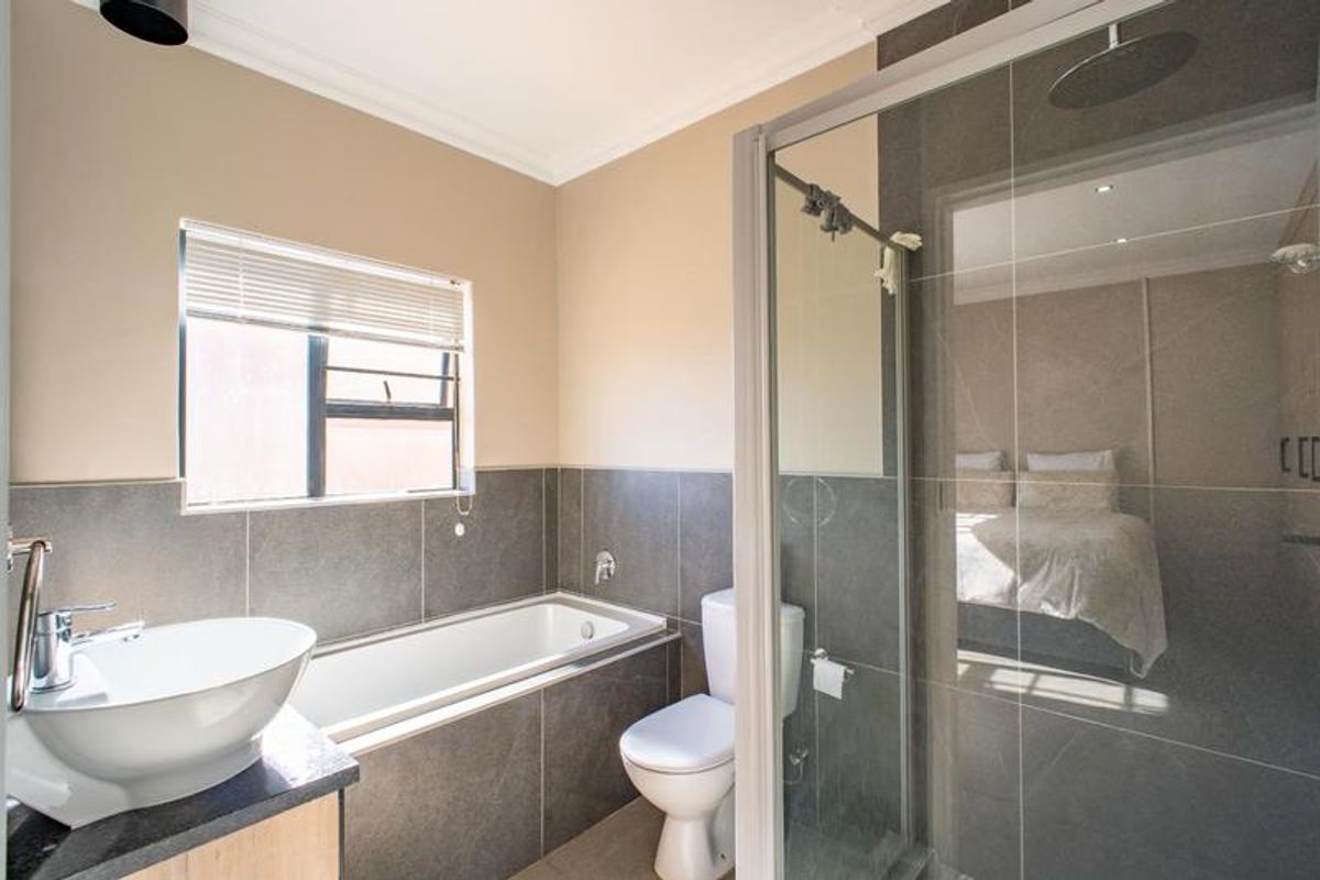 Modern bathroom featuring a vessel sink, built-in bathtub, and a separate glass-enclosed shower with contemporary grey wall tiling.