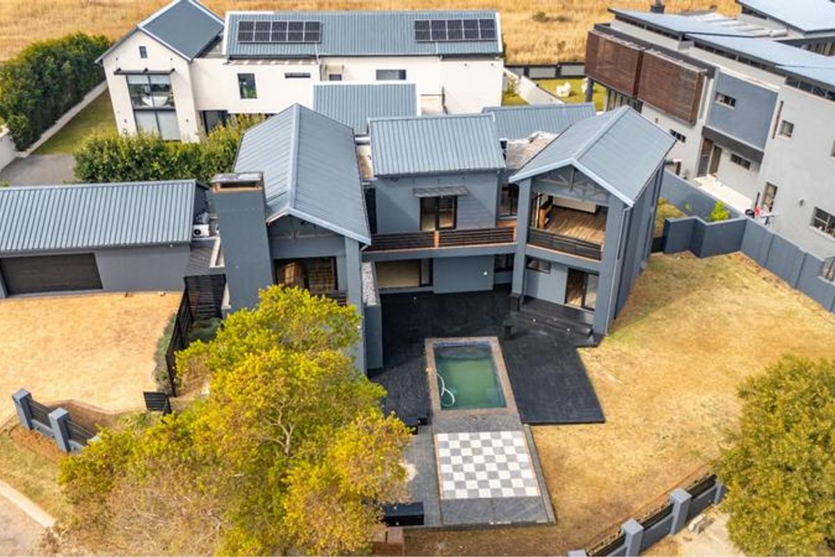 Aerial view of a modern multi-story house featuring a metal roof with solar panels, a swimming pool, and a paved outdoor entertainment area.