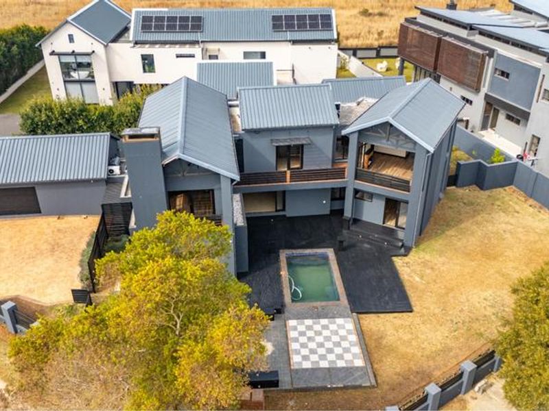 Aerial view of a modern multi-story house featuring a metal roof with solar panels, a swimming pool, and a paved outdoor entertainment area.
