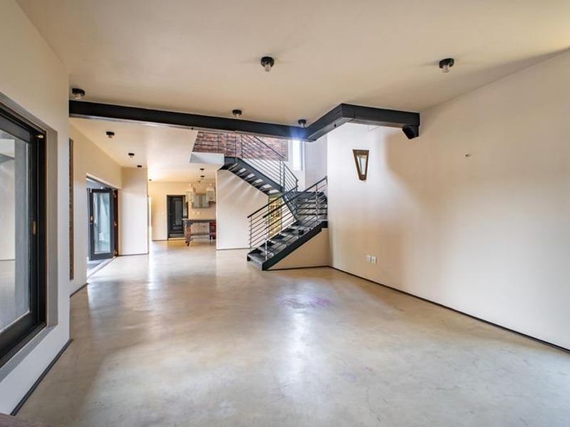 Spacious open-plan living area featuring polished concrete floors, an industrial-style steel staircase, and exposed structural beams with large sliding doors to the exterior.