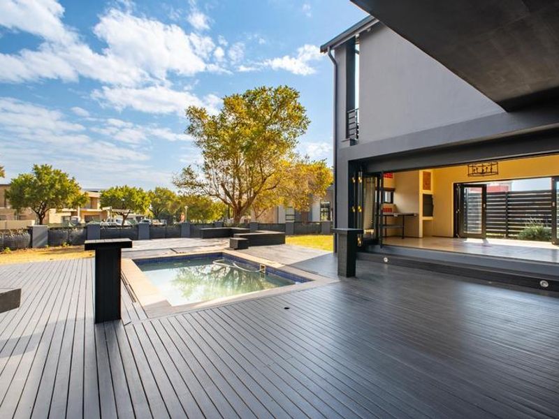 Modern outdoor entertainment area featuring a swimming pool, extensive composite decking, and seamless indoor-outdoor flow through large stacking doors.