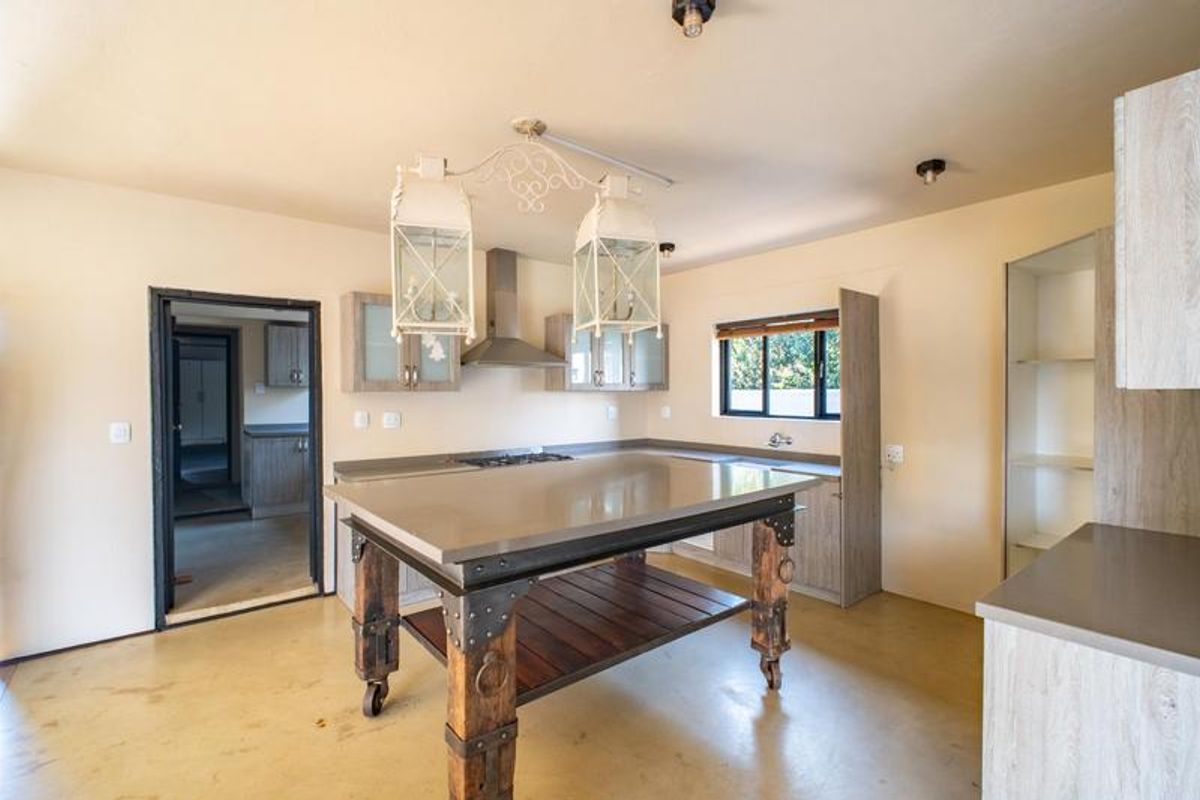 A spacious kitchen featuring light wood cabinetry, stone countertops, a central island, and a gas hob with an extractor fan.