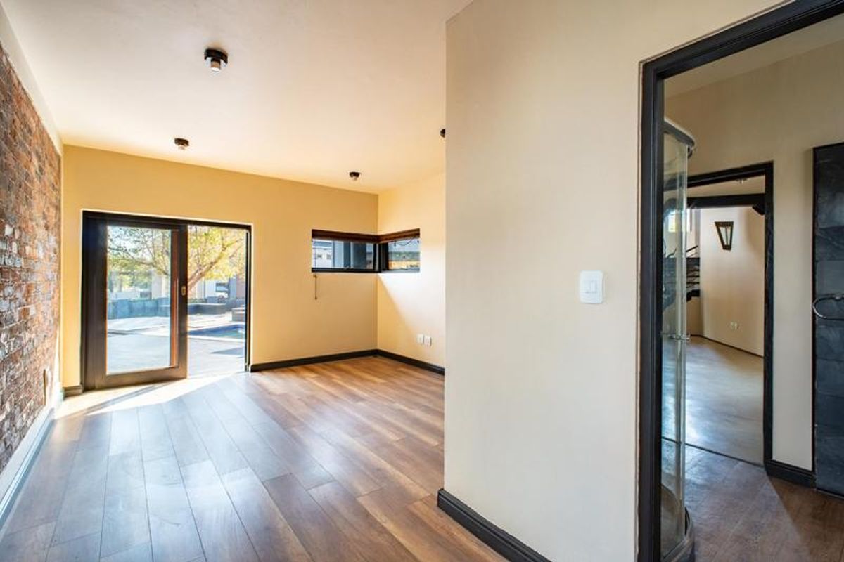 An empty living area featuring laminate flooring, an exposed brick feature wall, and a sliding door providing access to the outdoor pool area.