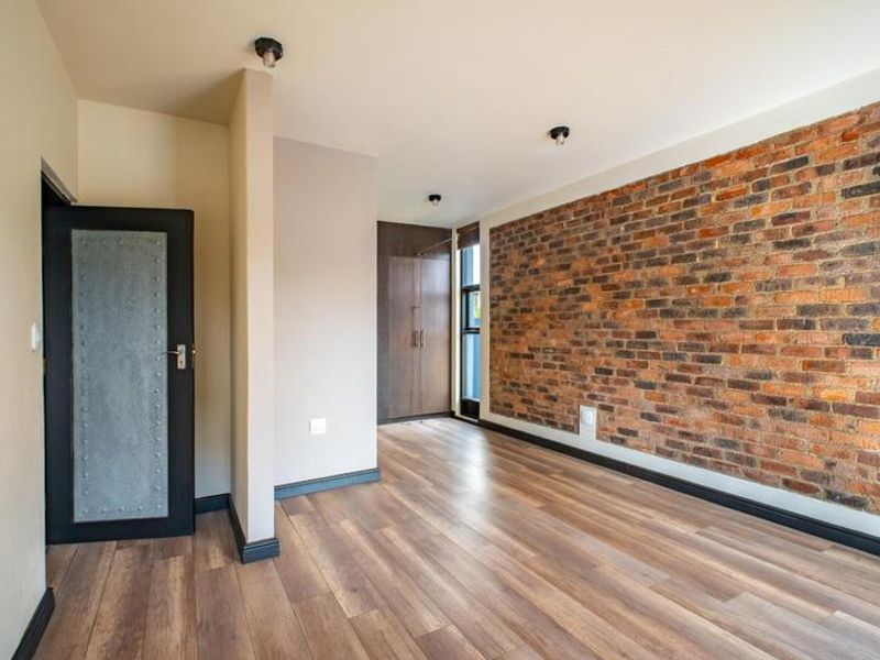 A modern, empty bedroom featuring an exposed brick feature wall, laminate flooring, and built-in storage cupboards.