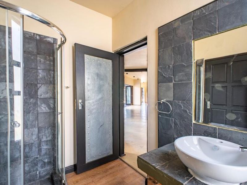 A modern bathroom featuring a glass shower enclosure, a vessel sink set on a stone vanity, and dark slate-style wall tiling.