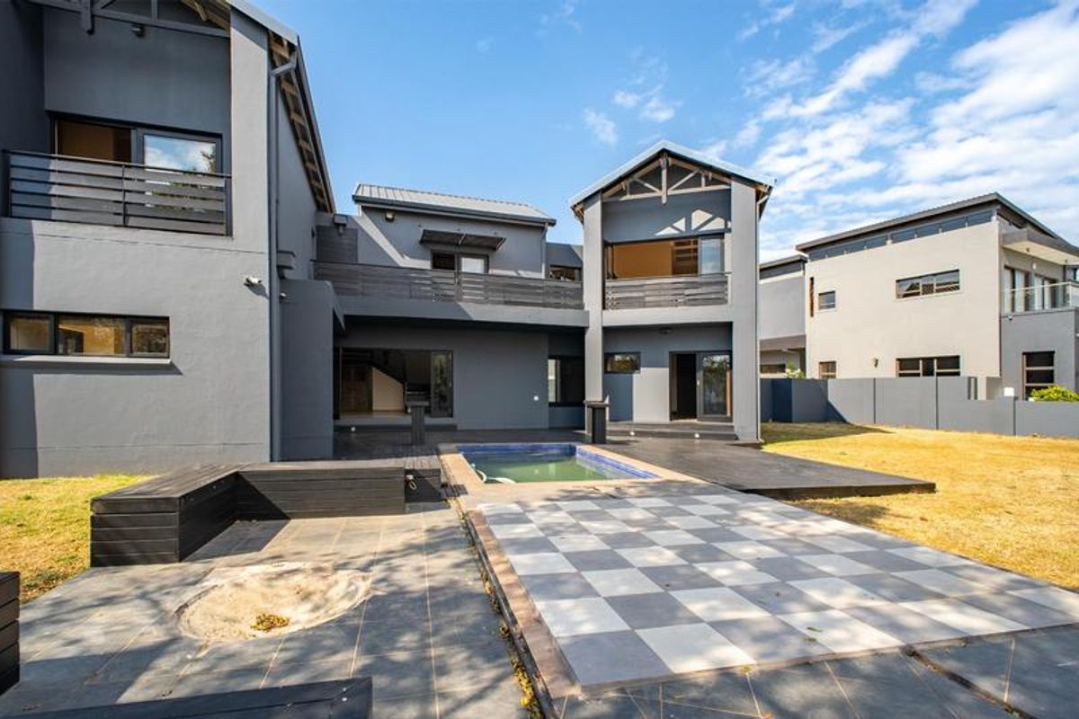 Rear view of a modern multi-story home featuring a swimming pool, tiled patio area, built-in seating, and upper-level balconies.