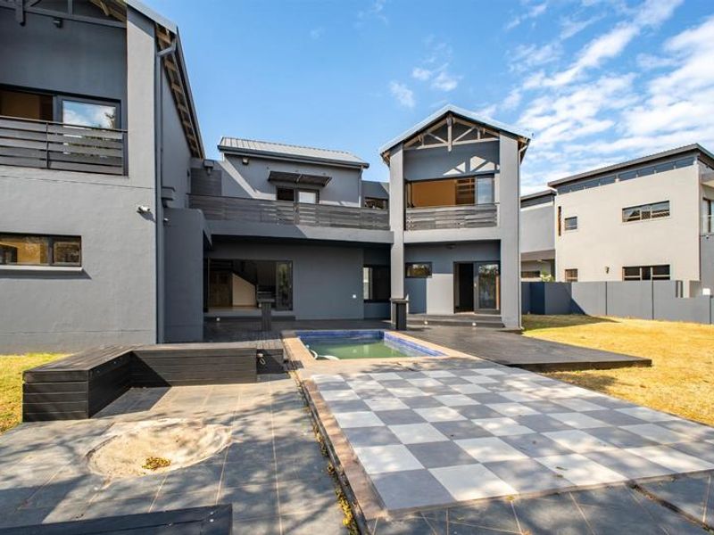 Rear view of a modern multi-story home featuring a swimming pool, tiled patio area, built-in seating, and upper-level balconies.