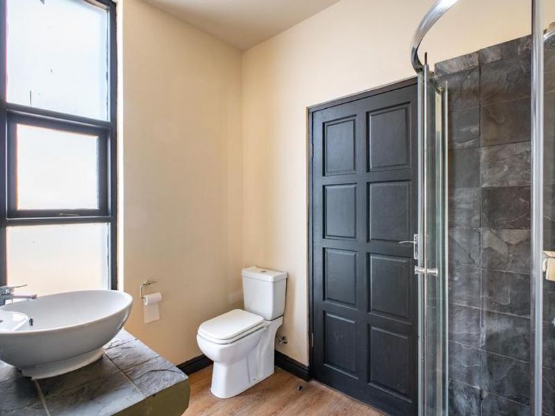 A modern bathroom featuring a vessel sink on a stone vanity, a toilet, and a glass-enclosed shower with dark slate tiling.