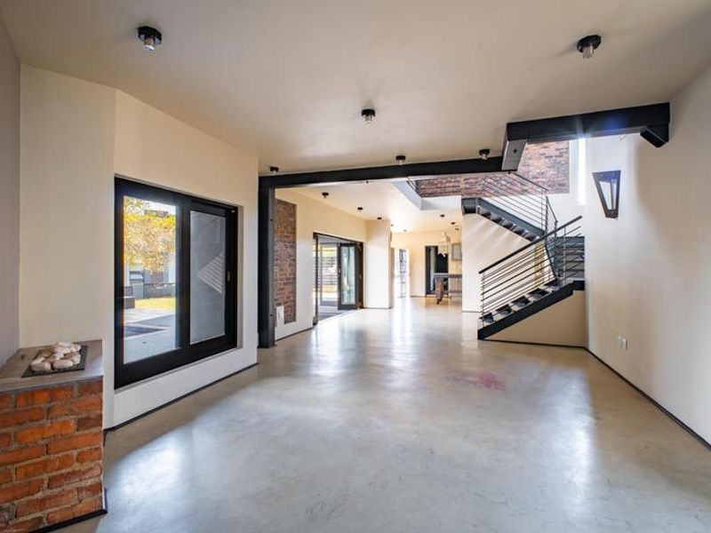 Spacious open-plan living area featuring polished concrete floors, exposed brick accents, and a modern steel staircase with industrial-style support beams.