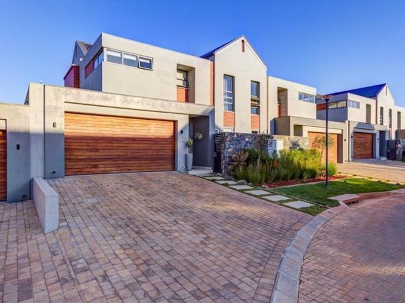 Modern townhouse exterior featuring a paved driveway, timber garage door, and stone-clad architectural details in a well-maintained residential estate setting.