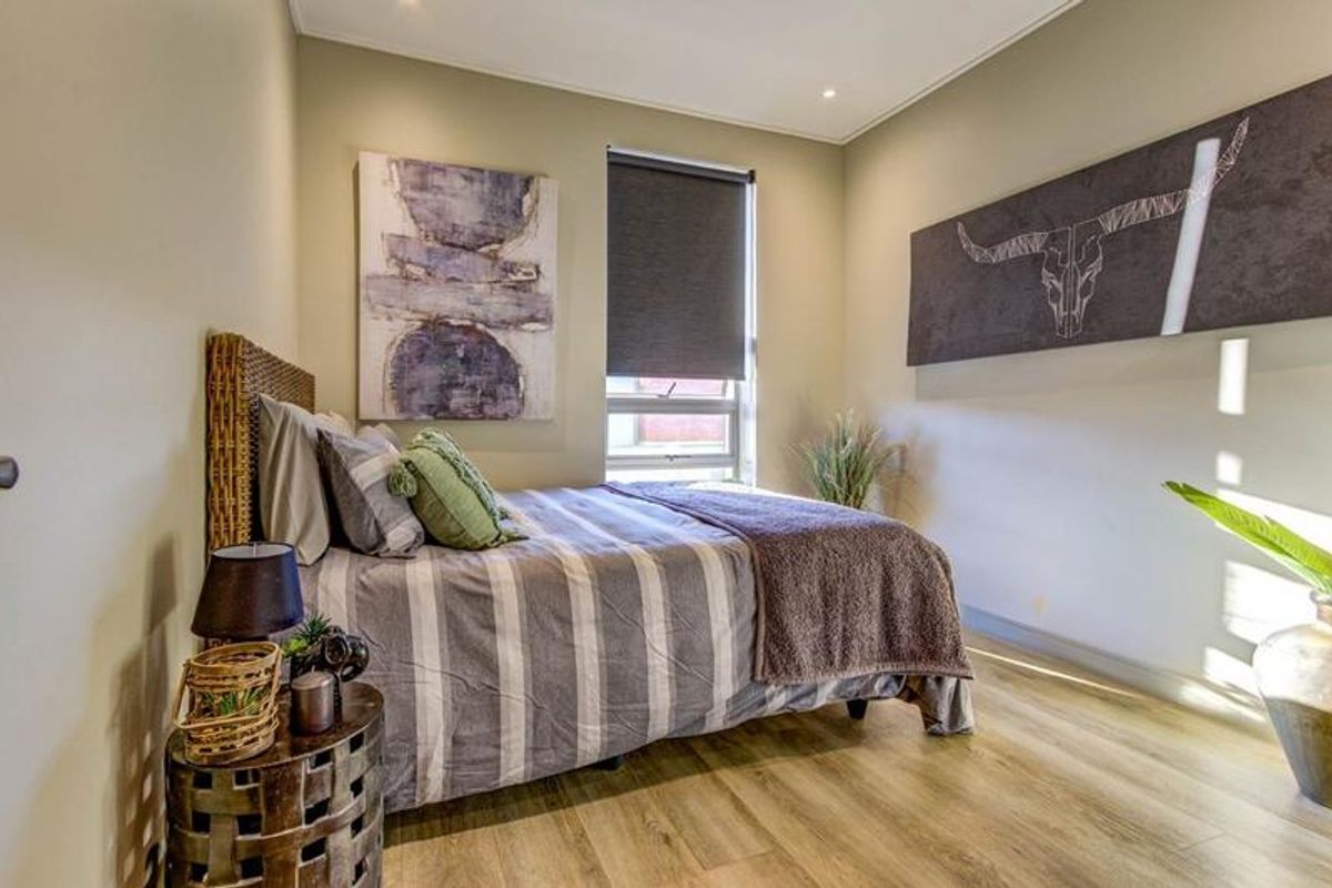 A well-maintained bedroom featuring modern laminate flooring, recessed downlighting, and a functional roller blind for privacy.