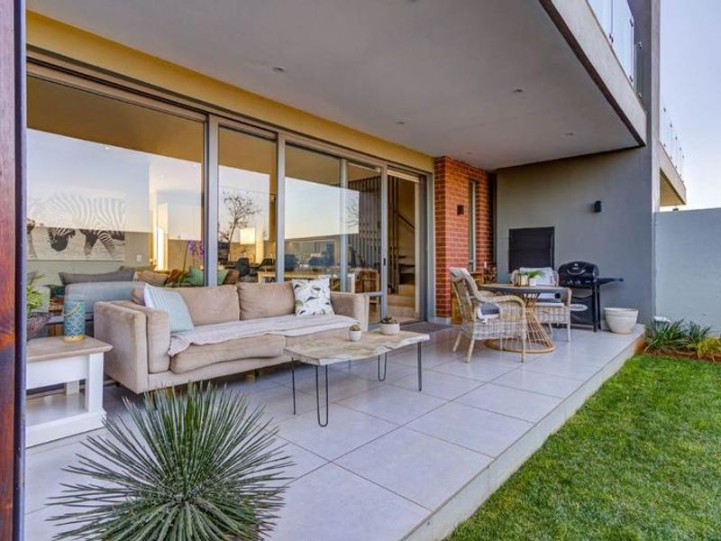 A covered patio featuring large format floor tiles, recessed lighting, and a built-in braai, seamlessly connecting to the interior living space via sliding doors.