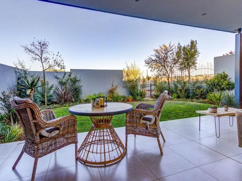A covered patio featuring tiled flooring and recessed lighting, overlooking a private landscaped garden with boundary walls.