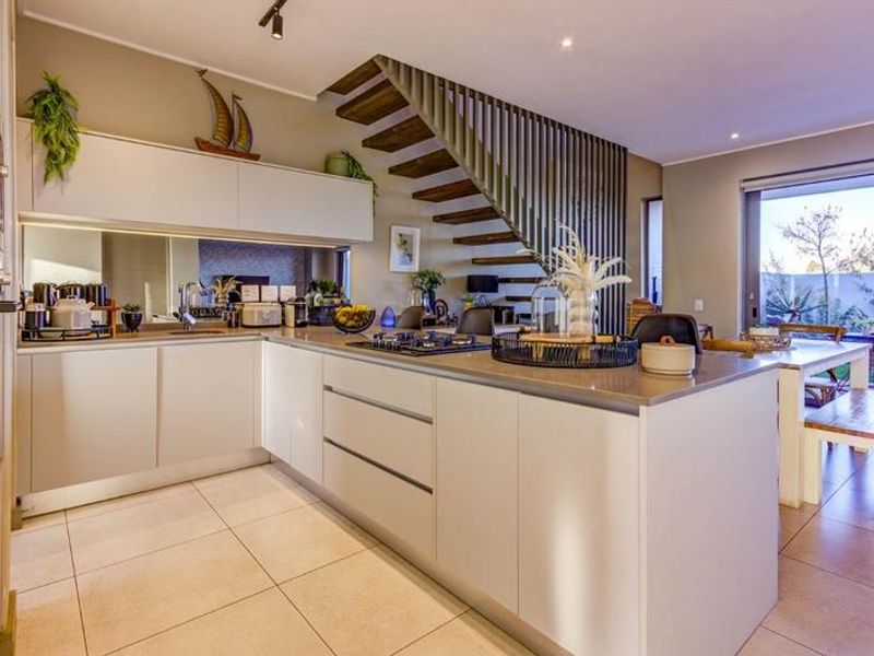 Modern open-plan kitchen featuring sleek cabinetry, a central island with a gas cooktop, and a striking staircase with a contemporary vertical slat balustrade.