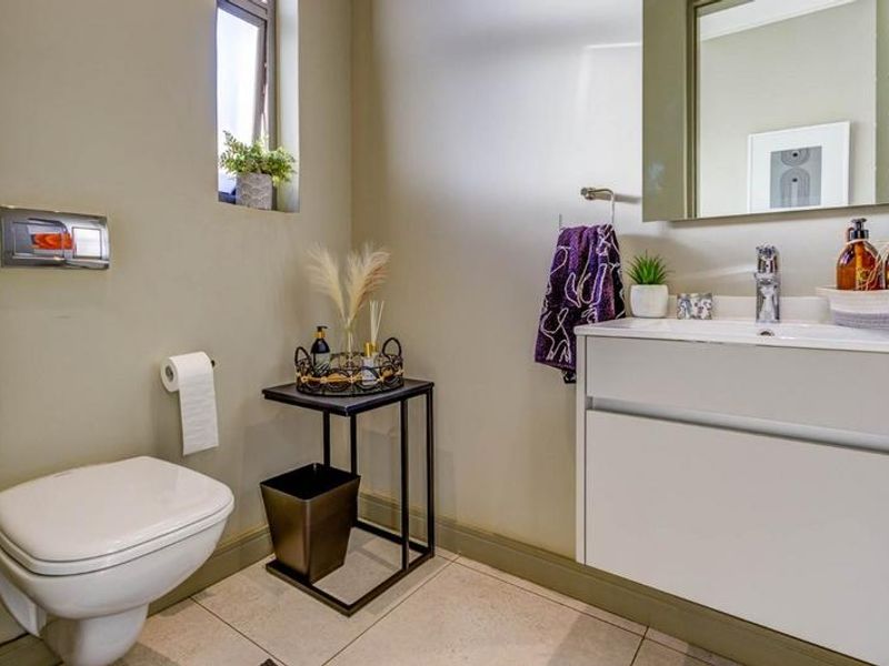 A modern guest bathroom featuring a wall-mounted toilet with a concealed cistern, a sleek vanity cabinet with a basin, and neutral tiled flooring.