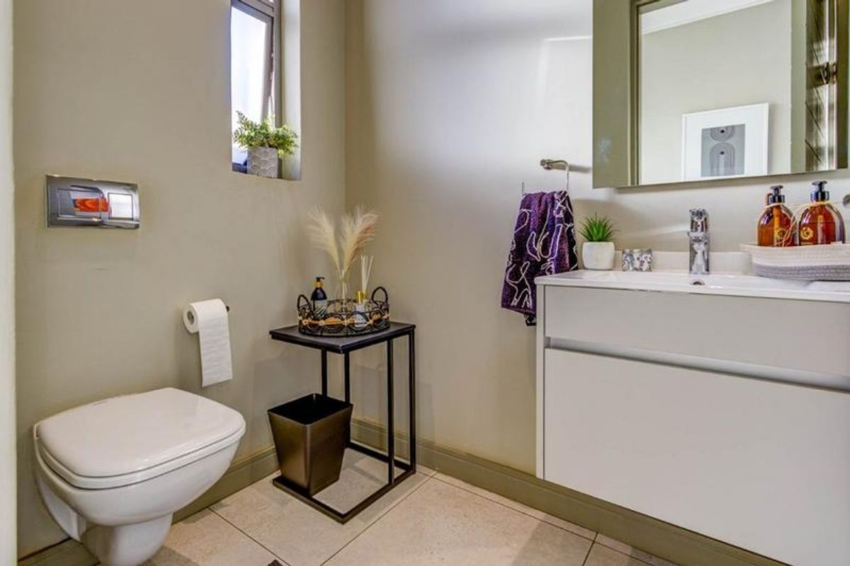 A modern guest bathroom featuring a wall-mounted toilet with a concealed cistern, a sleek vanity cabinet with a basin, and neutral tiled flooring.