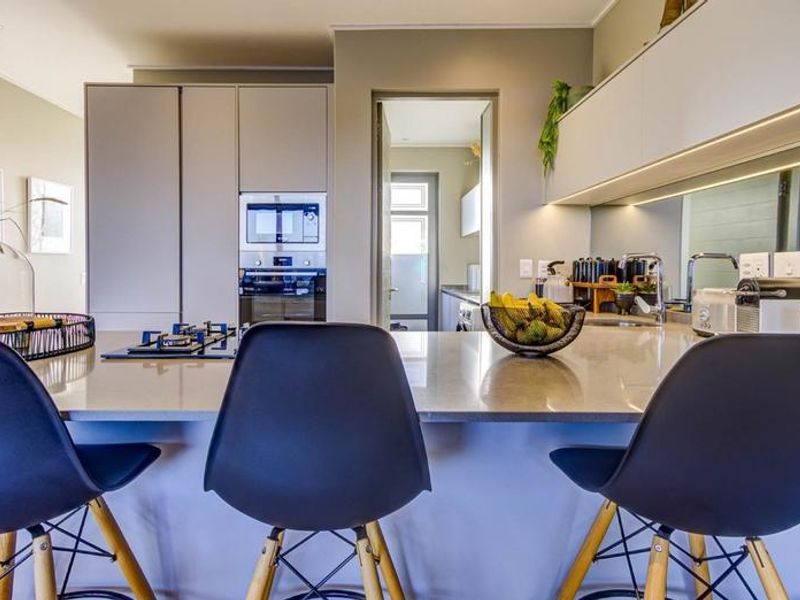 Modern kitchen featuring a stone island, built-in appliances, mirrored splashback, and sleek cabinetry with integrated lighting.