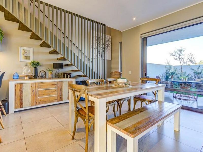 Open-plan dining area featuring modern tiled flooring, a striking staircase with vertical balustrades, and large sliding glass doors opening to a private patio.