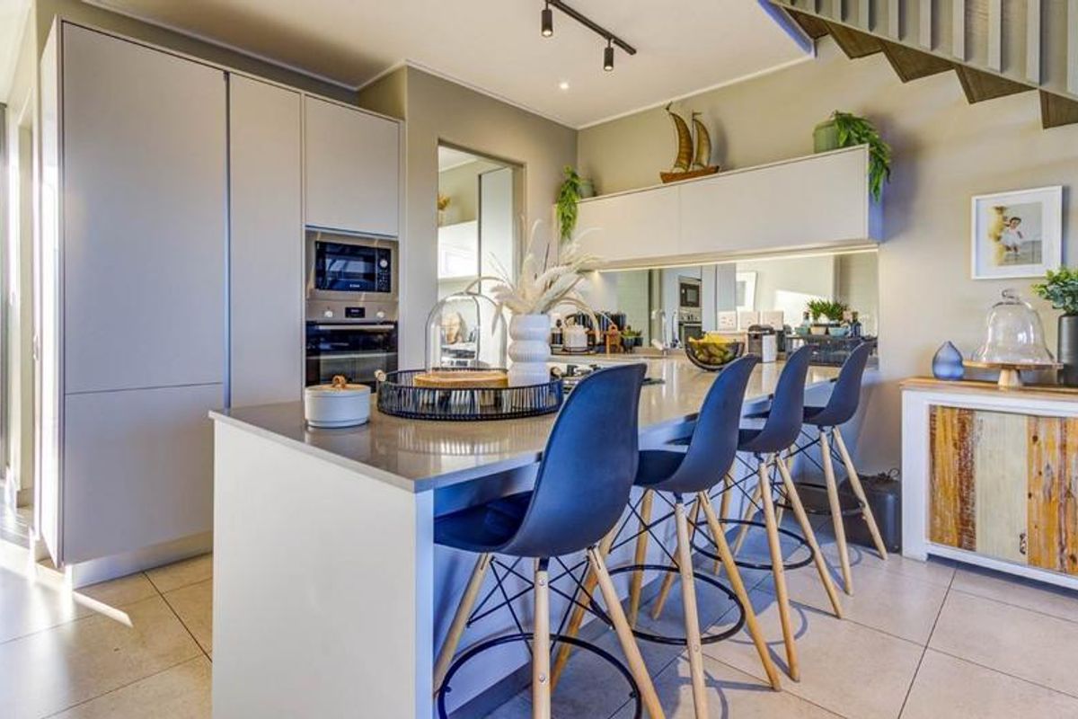 Modern kitchen featuring a central island with stone countertops, built-in oven and microwave, mirrored backsplash, and sleek cabinetry, adjacent to a staircase.