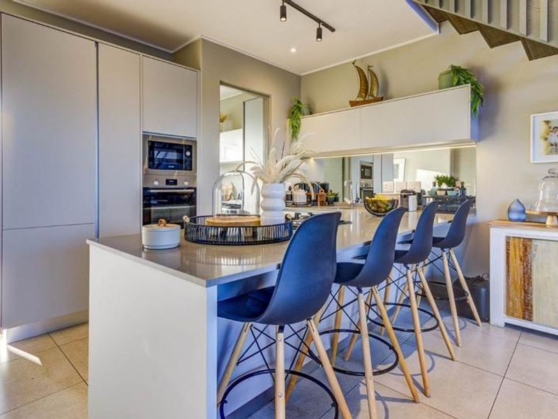 Modern kitchen featuring a central island with stone countertops, built-in oven and microwave, mirrored backsplash, and sleek cabinetry, adjacent to a staircase.