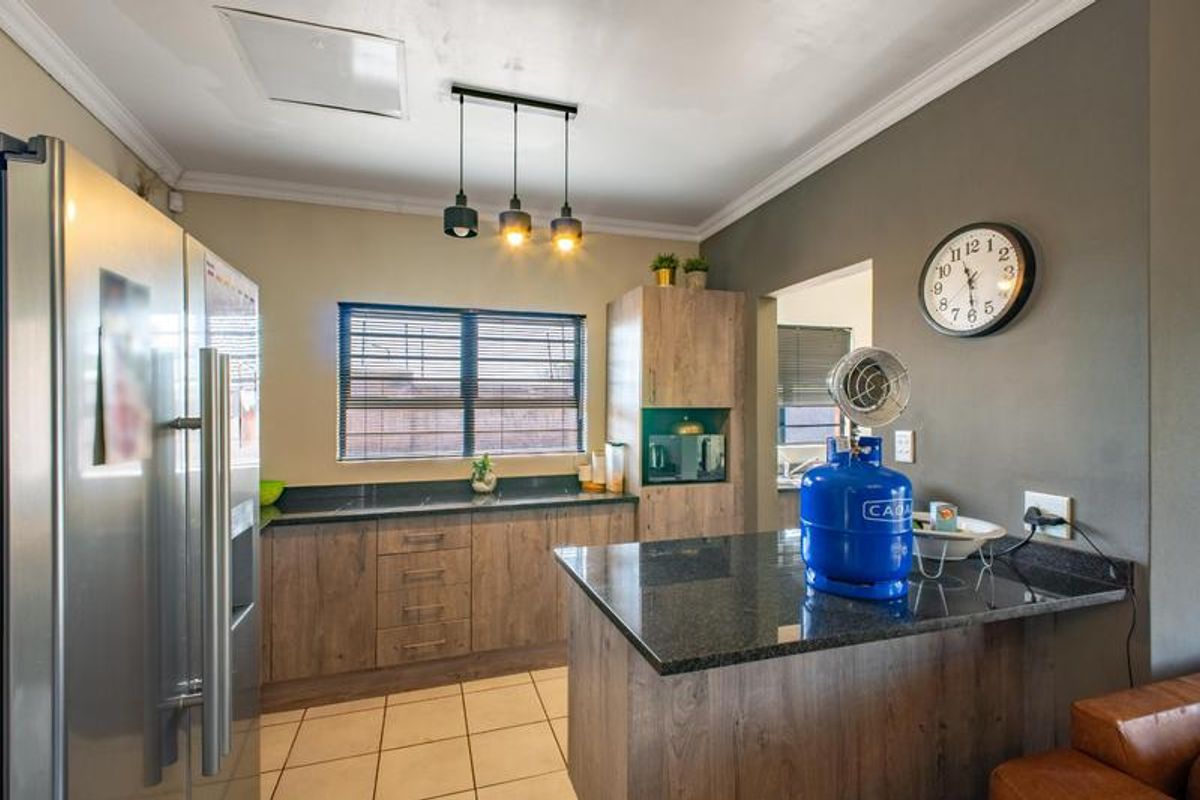 Modern kitchen featuring wood-look cabinetry, dark granite countertops, tiled flooring, and a functional breakfast bar area with pendant lighting.