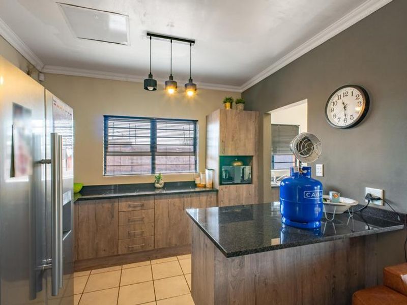 Modern kitchen featuring wood-look cabinetry, dark granite countertops, tiled flooring, and a functional breakfast bar area with pendant lighting.