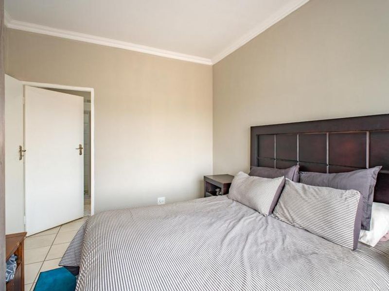 A bedroom featuring tiled flooring, coving, and a built-in wardrobe, with an adjacent en-suite bathroom visible through the doorway.