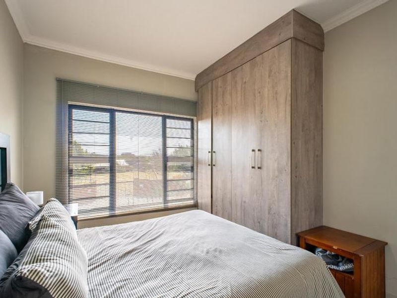 A well-maintained bedroom featuring a large built-in wardrobe with wood-grain finish, aluminium window frames, and fitted venetian blinds.