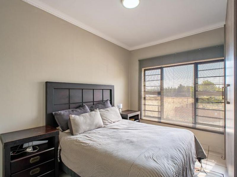 A well-maintained bedroom featuring built-in cupboards, tiled flooring, and large windows with venetian blinds, offering a clean and functional living space.