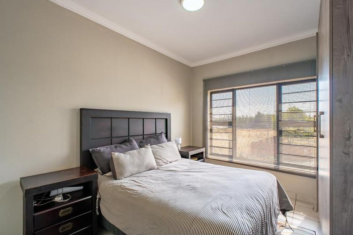 A well-maintained bedroom featuring built-in cupboards, tiled flooring, and large windows with venetian blinds, offering a clean and functional living space.