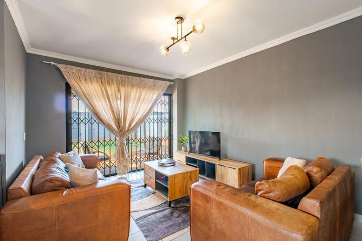 A well-maintained living room featuring crown molding, a modern light fixture, and a security gate leading to the outdoor area.