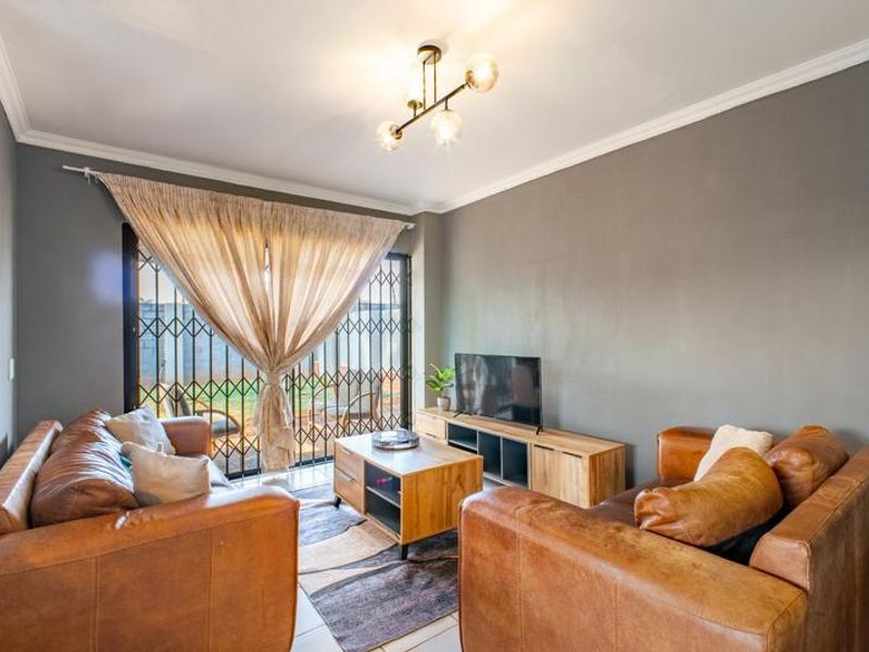 A well-maintained living room featuring crown molding, a modern light fixture, and a security gate leading to the outdoor area.