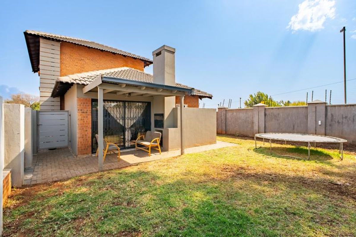 Rear view of the townhouse featuring a covered patio with a built-in braai, paved area, and a private garden with perimeter walling.