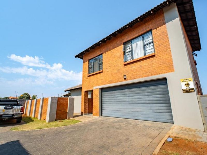 A well-maintained double-story townhouse featuring a face-brick exterior, a paved driveway, and an automated garage door.