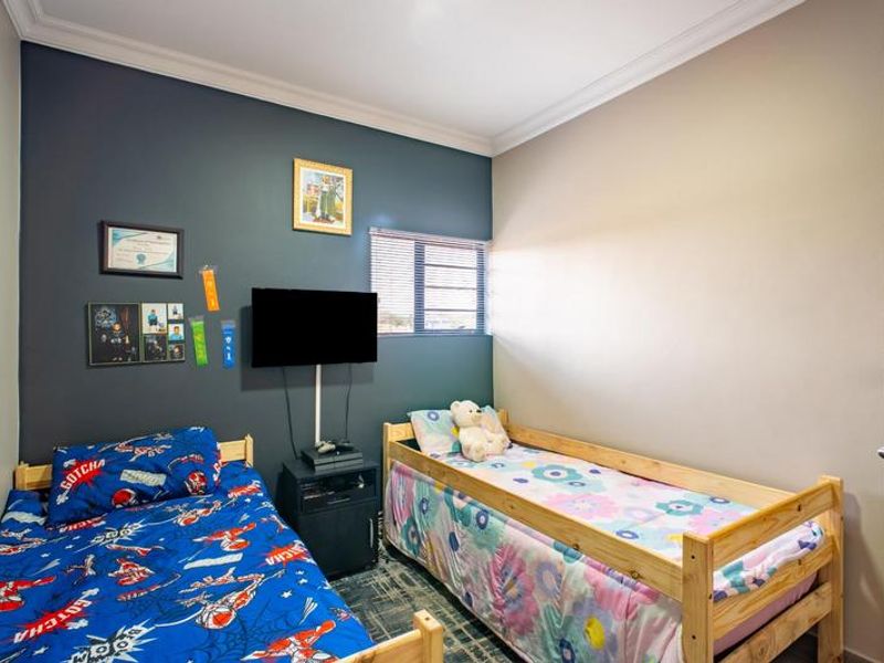 A compact bedroom featuring a dark accent wall, neutral side walls, and a window with fitted blinds.