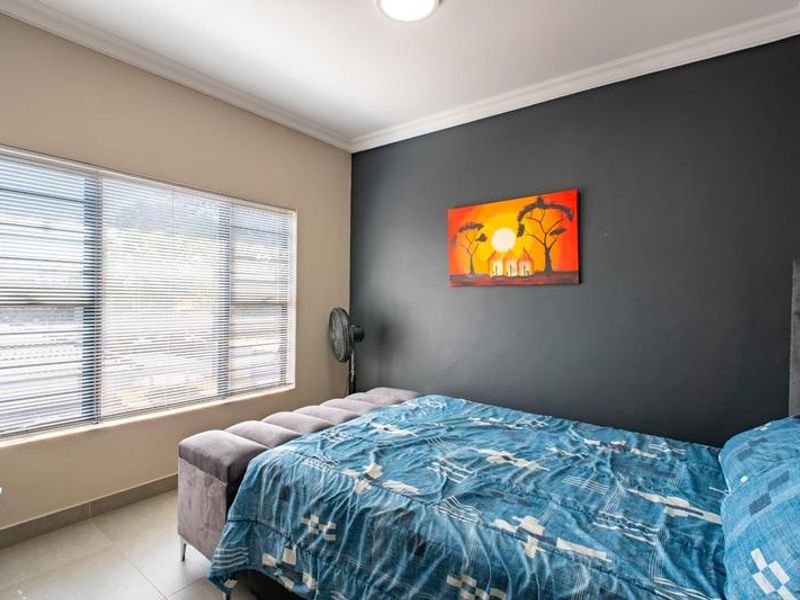 A well-maintained bedroom featuring tiled flooring, neutral wall tones with a dark accent wall, and fitted venetian blinds.