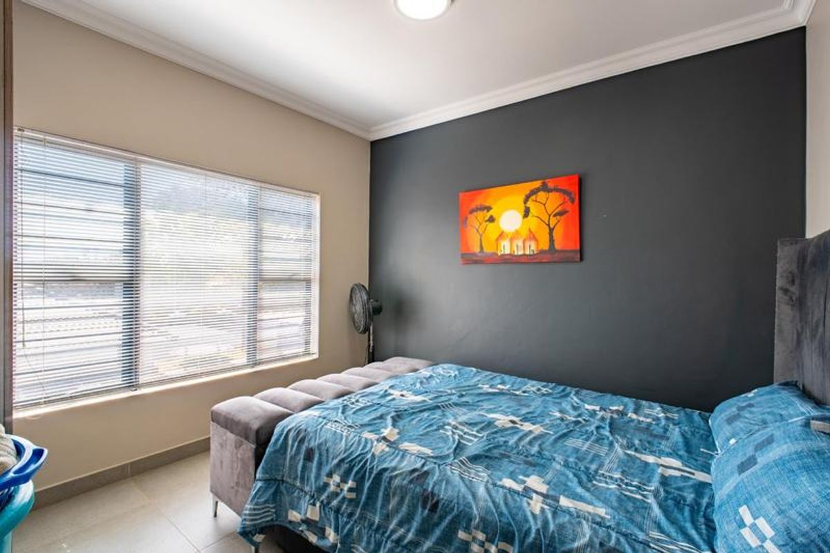 A well-maintained bedroom featuring tiled flooring, neutral wall tones with a dark accent wall, and fitted venetian blinds.