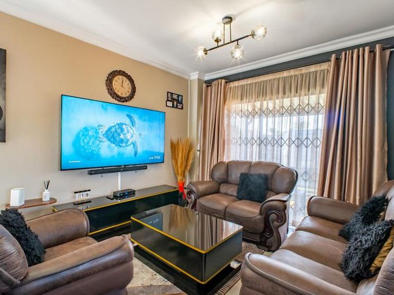 A well-maintained living room featuring crown molding, a modern ceiling light fixture, and a sliding glass door with an integrated security gate.
