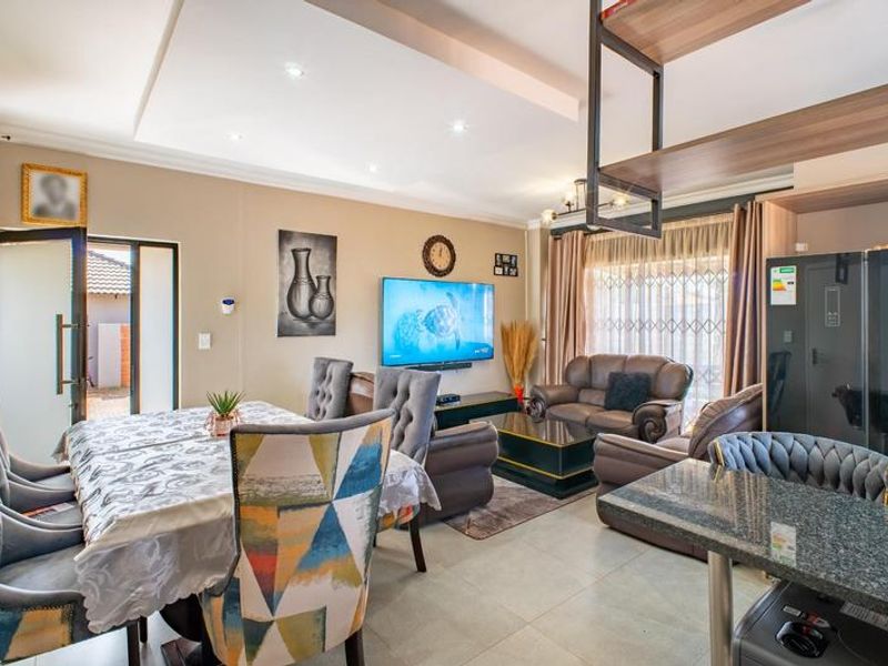 An open-plan living and dining area featuring a coffered ceiling with recessed lighting, tiled floors, and a granite kitchen counter.