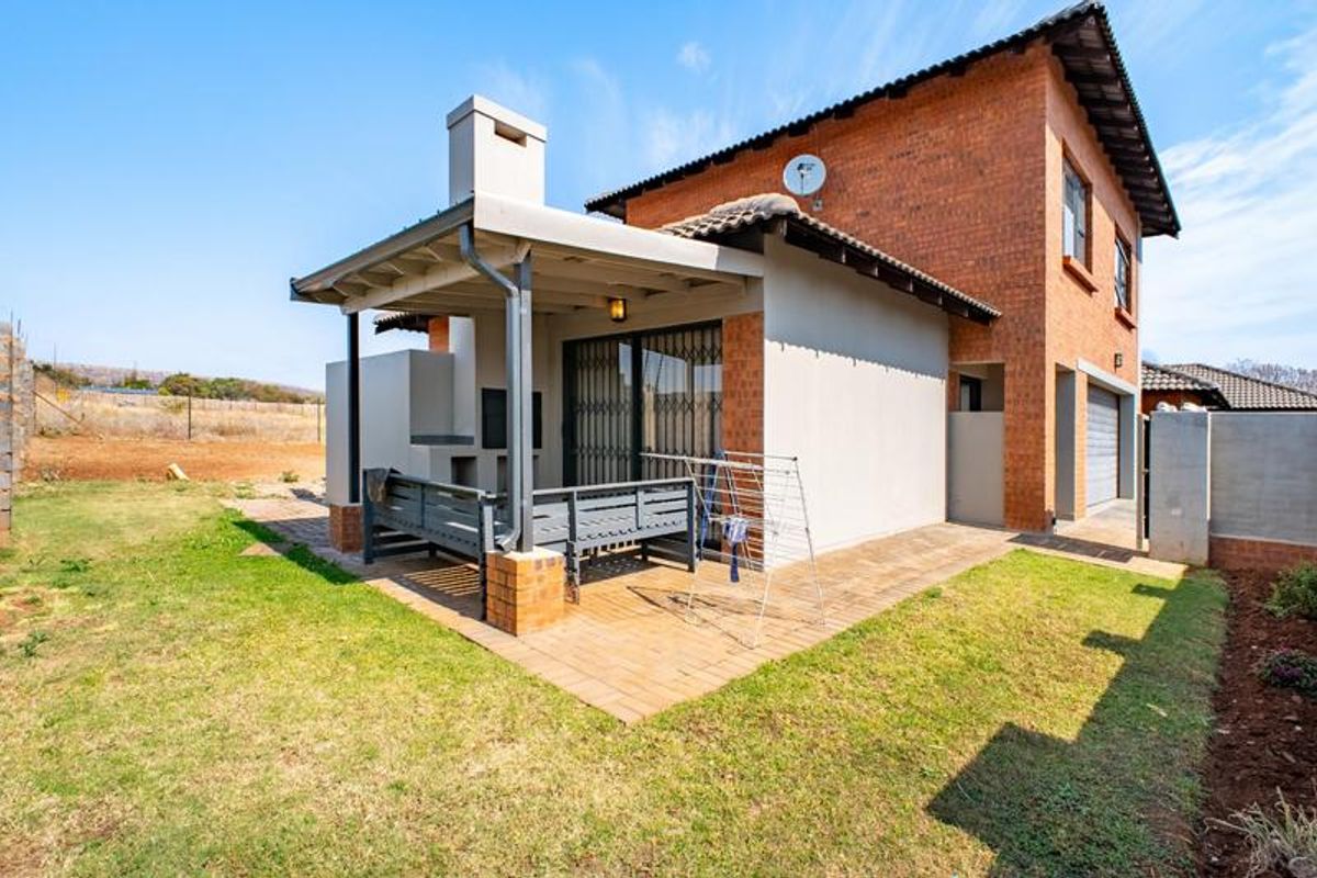 Rear view of the townhouse featuring a covered patio with a built-in braai, brick paving, and access to the garden area.