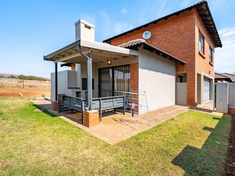 Rear view of the townhouse featuring a covered patio with a built-in braai, brick paving, and access to the garden area.
