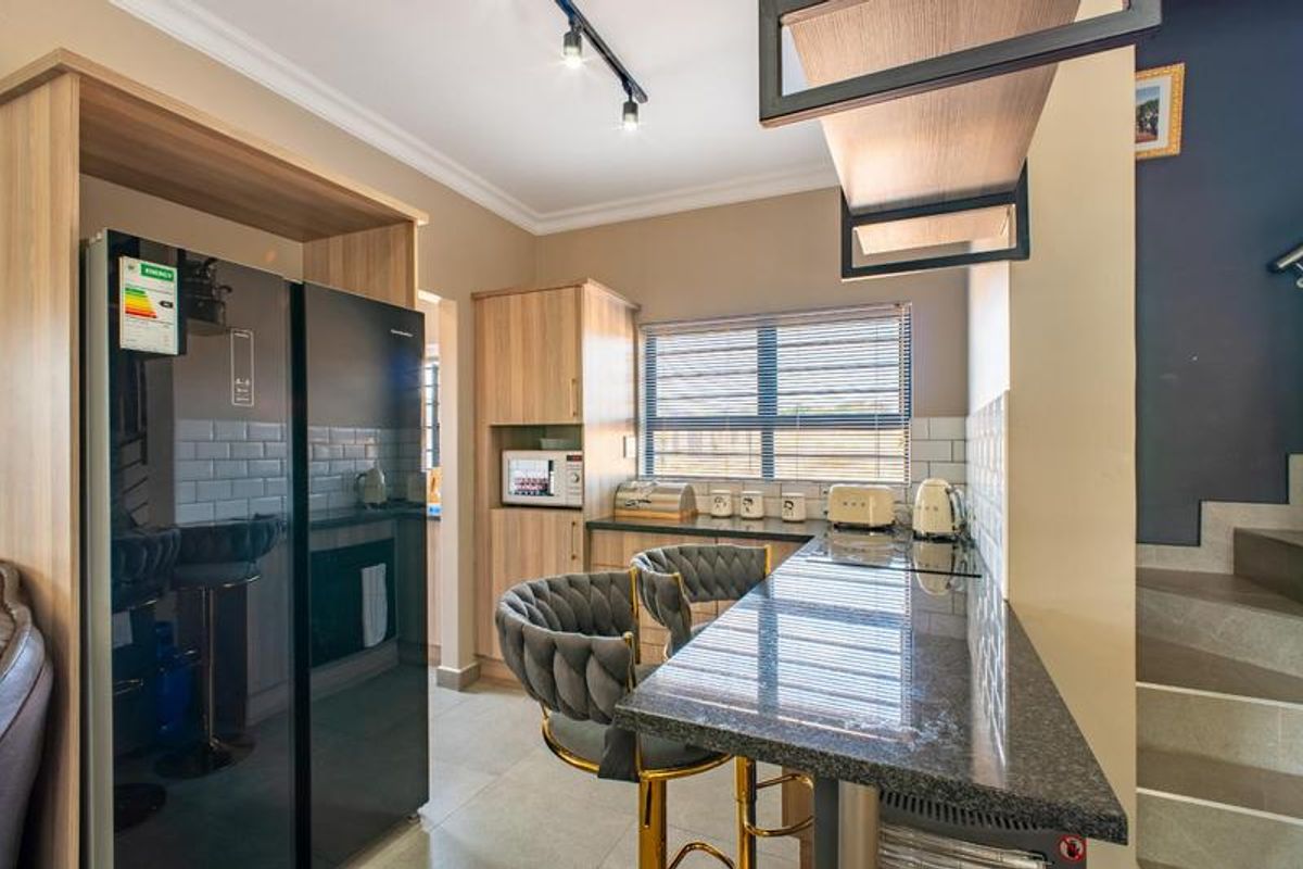 Modern kitchen featuring wood-finish cabinetry, stone countertops, subway tile backsplash, and a breakfast bar, adjacent to a staircase.