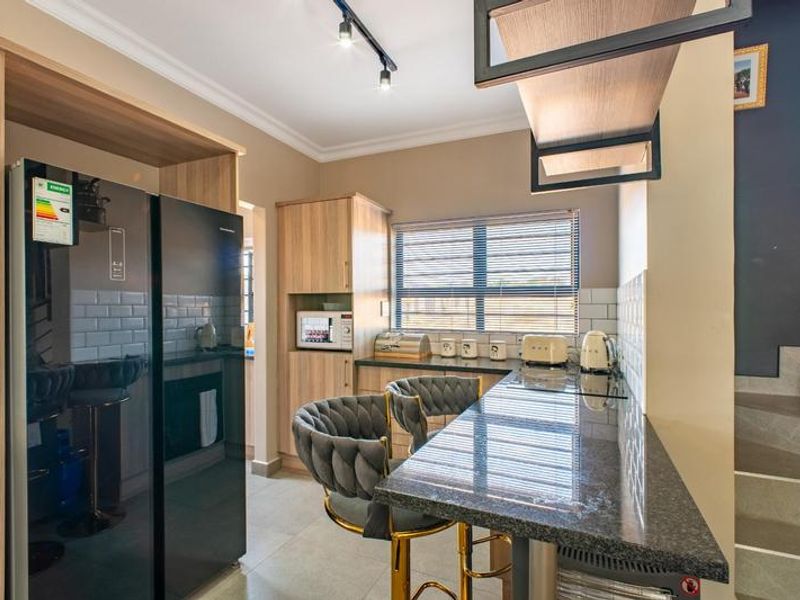 Modern kitchen featuring wood-finish cabinetry, stone countertops, subway tile backsplash, and a breakfast bar, adjacent to a staircase.