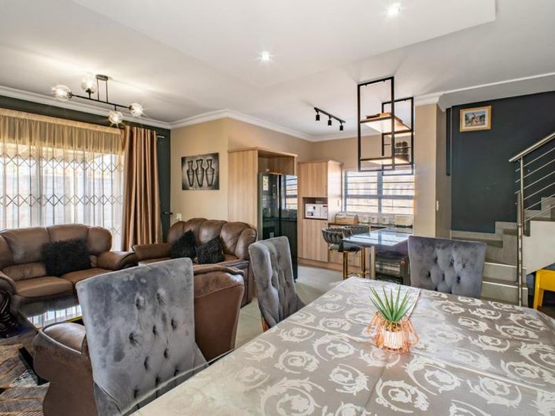 Spacious open-plan living and dining area featuring modern cabinetry, a staircase with metal balustrades, and tiled flooring throughout.