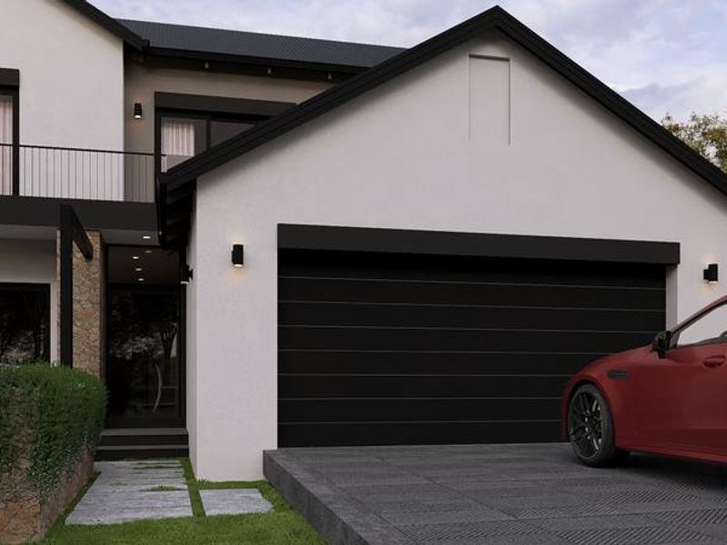 Modern double-story residential facade featuring a sleek black garage door, stone accent wall, and an upper-level balcony with contemporary metal railings.