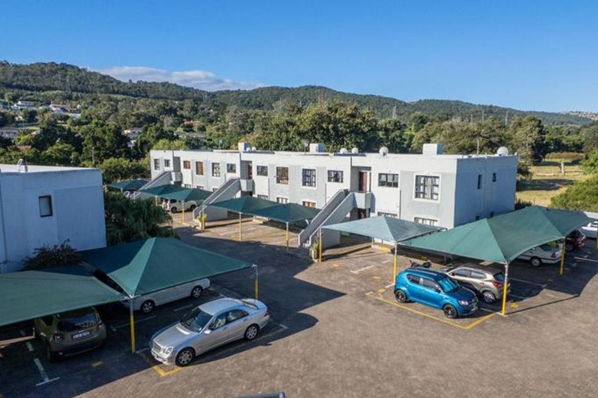 Aerial view of an apartment complex featuring a paved parking area with multiple shade cloth carports and external building access staircases.