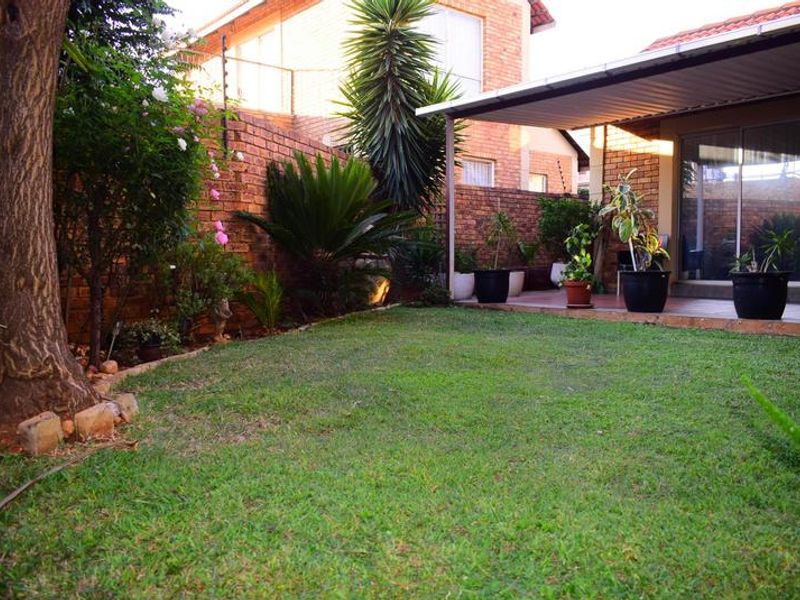 A private rear garden featuring a well-maintained lawn, established landscaping, and a covered patio area with direct access to the home via sliding doors.